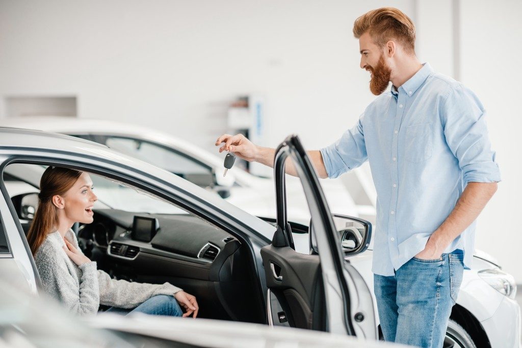 suprised woman and husband handing keys to new car