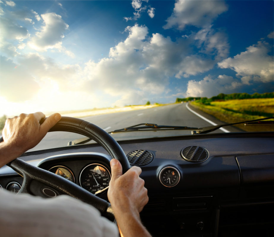 Hands of a driver on steering wheel of a car and empty asphalt road