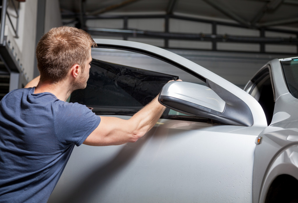 A man in blue t shirt installing tinting foil on his car window
