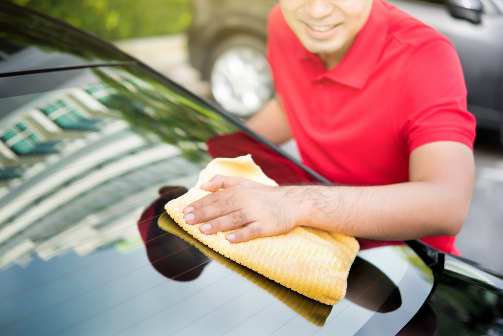 Man wearing red t shirt cleaning windshield with a soft cloth 