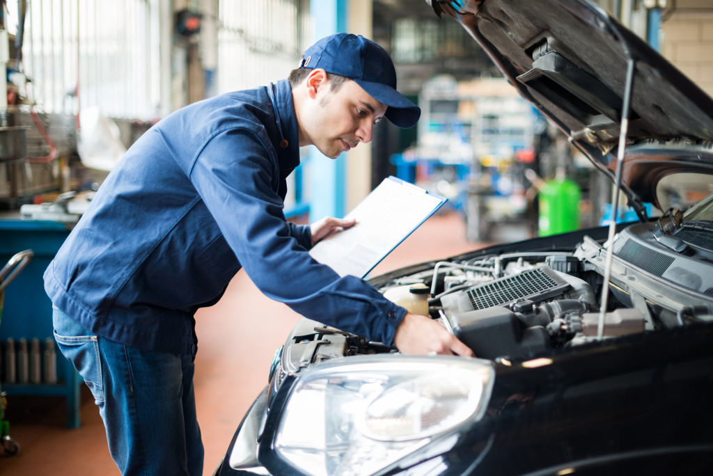 male mechanic wearing blue overalls fixing black car opened up